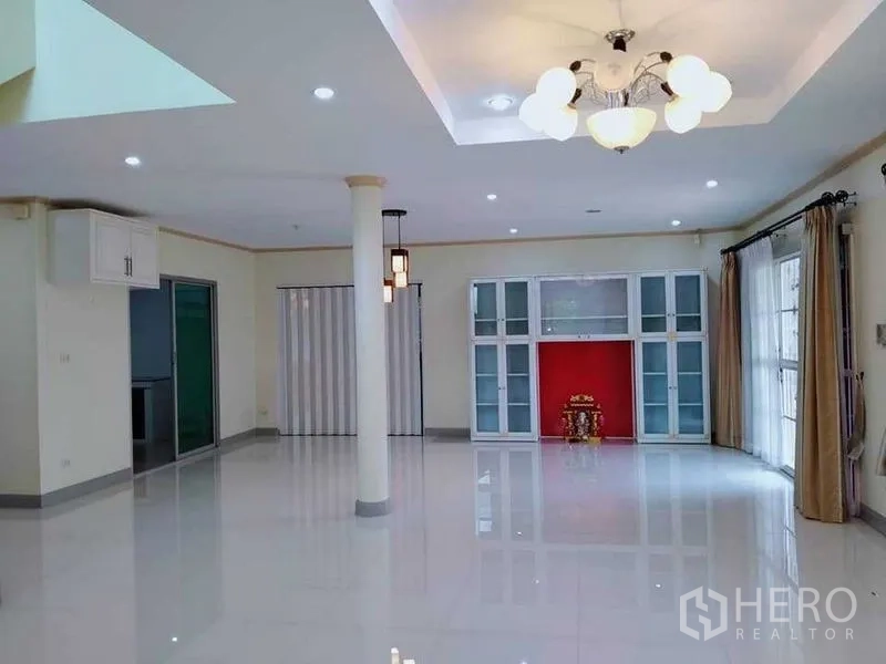 Detached House for sale in Phasi Charoen, Bangkok - Open‑plan living room with columns, chandelier lighting, large windows, and built‑in display shelving.