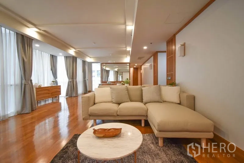 คอนโด ให้เช่าในPathum Wan, Bangkok - ห้องนั่งเล่นโปร่งสว่าง โซฟารูป L โต๊ะกลางหินอ่อน และผ้าม่านสูงจรดเพดาน