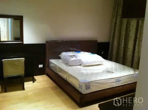 Condominium for rent in Pathum Wan, Bangkok - Cozy bedroom with double bed, wooden flooring, desk with mirror, and patterned blackout curtains.