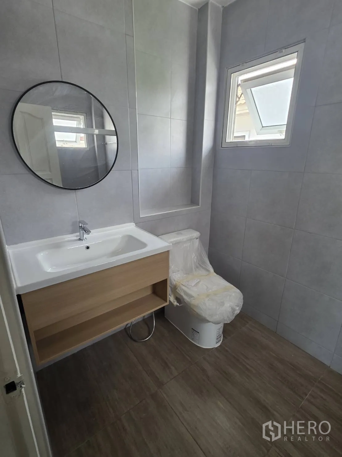 Detached House for sale in Lam Luk Ka, Pathum Thani - Bathroom with round mirror, floating wood vanity, and toilet on gray tile.