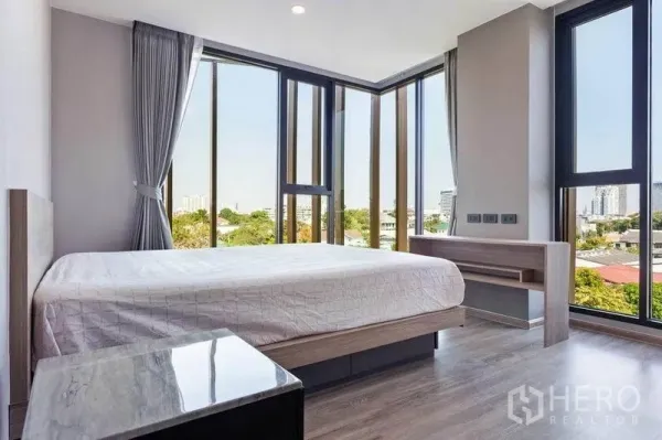 Condominium for rent or sale in Watthana, Bangkok - Corner master bedroom with wraparound windows, city and treetop views, plus a built-in desk.