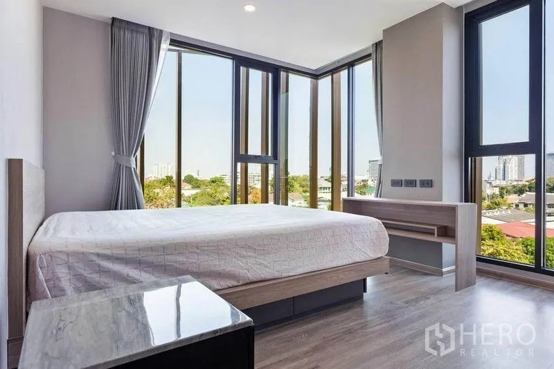 Condominium for rent or sale in Watthana, Bangkok - Corner master bedroom with wraparound windows, city and treetop views, plus a built-in desk.