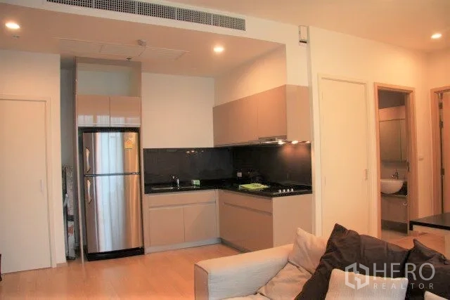 Condominium for rent in Watthana, Bangkok - Modern L-shaped kitchen with stainless refrigerator, black stone counters and cooktop beside the lounge.