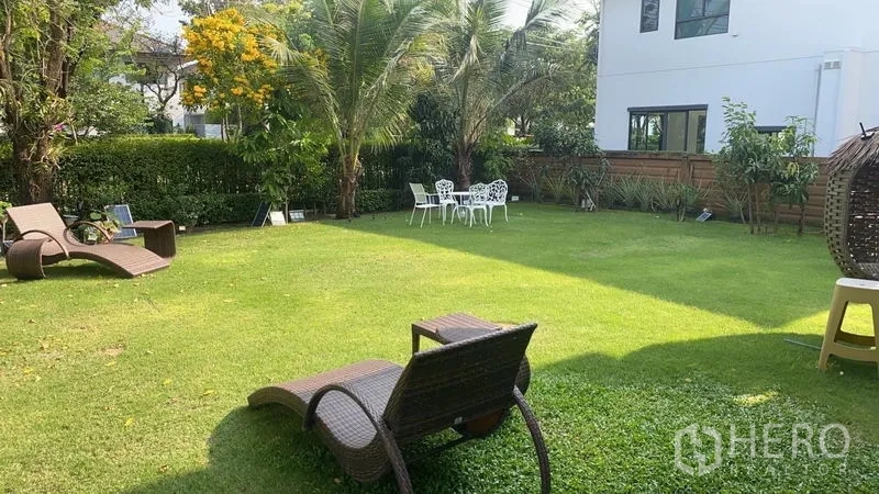 Detached House for rent or sale in Prawet, Bangkok - Large landscaped backyard lawn with palm trees, lounge chairs, and outdoor seating.