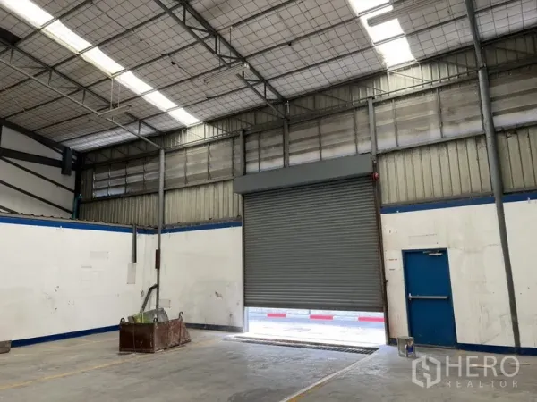 Warehouse for rent in Suan Luang, Bangkok - Interior view of the loading bay with a roll-up shutter and an emergency exit door.
