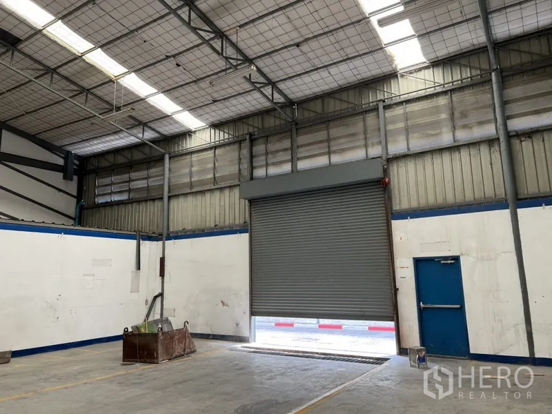 Warehouse for rent in Suan Luang, Bangkok - Interior view of the loading bay with a roll-up shutter and an emergency exit door.