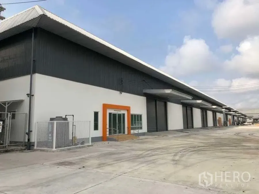 Factory for rent in Bang Sao Thong, Samut Prakan - Modern factory exterior with long loading bays, roller shutters and an office entrance in Bang Sao Thong.