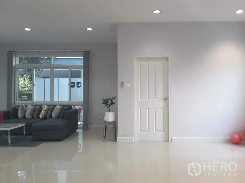 บ้าน ให้เช่าในLam Luk Ka, Pathum Thani - ห้องนั่งเล่นกว้าง โซฟาแอลสีเทาข้างหน้าต่างบานใหญ่ โทนสีเรียบ