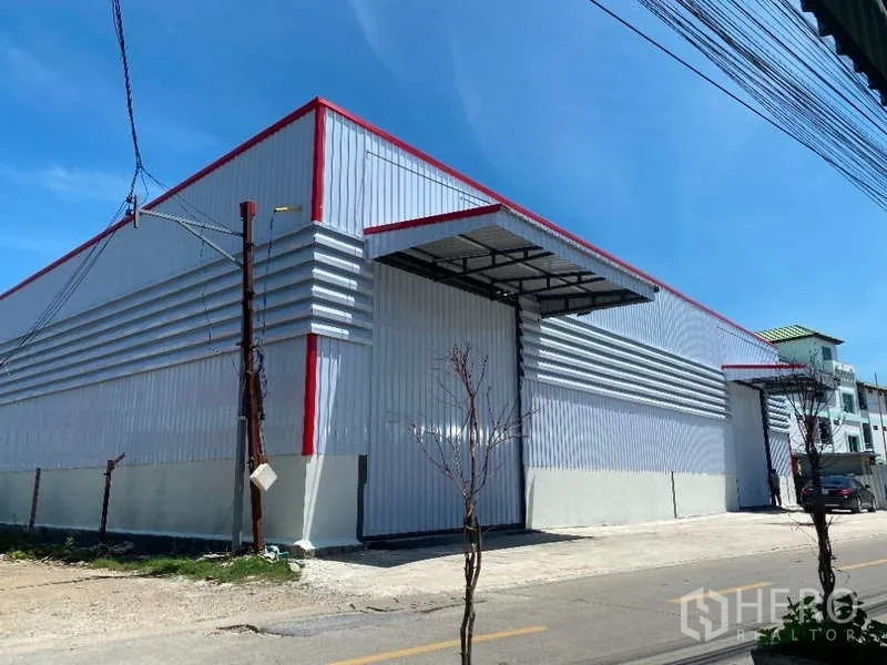 Warehouse for rent in Don Mueang, Bangkok - Long-span warehouse exterior with red roof trim and a covered awning over the loading entrance.