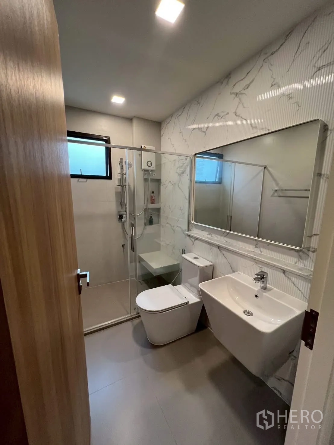 Detached House for rent in Samut Prakan - Contemporary bathroom with marble-style accent wall and glass shower.