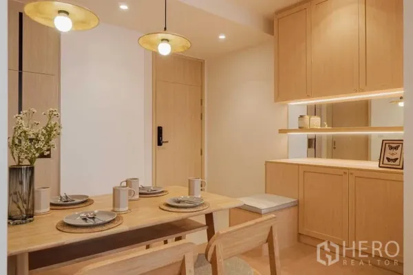 Condominium for rent in Watthana, Bangkok - Warm-toned dining area with wooden table, pendant lights and built-in cabinet with mirror.