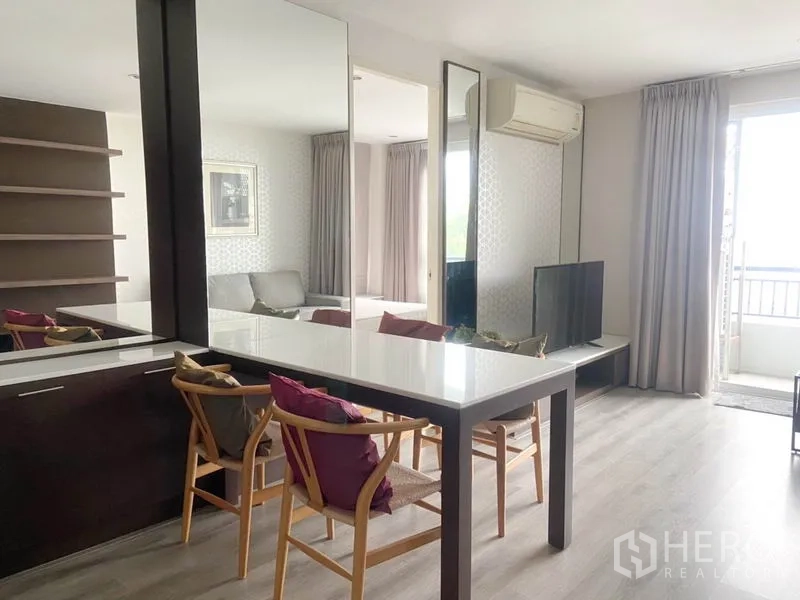 Condominium for rent in Watthana, Bangkok - Dining area with white table, wooden chairs, and mirrored panels opening toward the balcony.