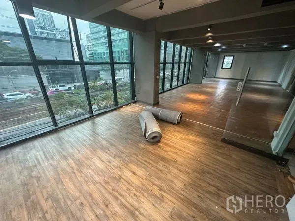 办公空间 出租在Bang Rak, Bangkok - 明亮开放空间，落地窗俯瞰城市街景，地上放置卷起的地毯。