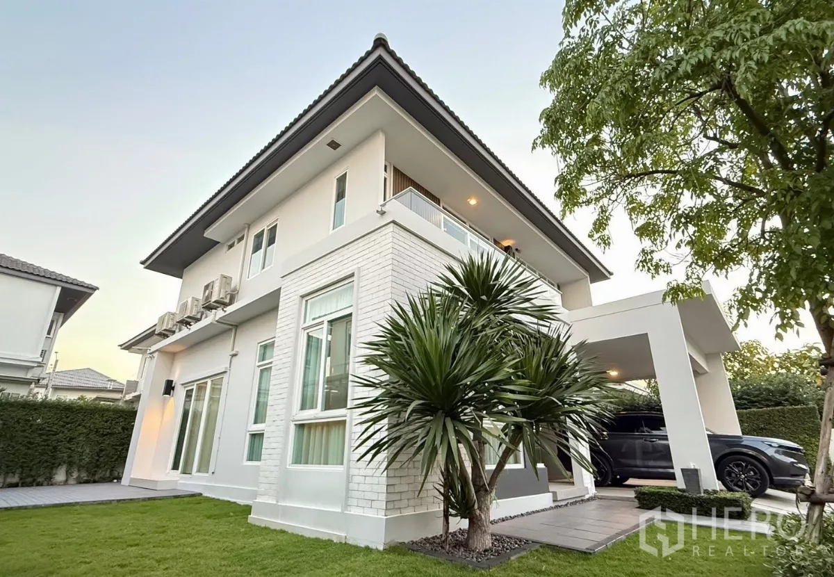 Detached House for rent in Prawet, Bangkok - Corner view of white two-storey house with balcony, carport and landscaped lawn