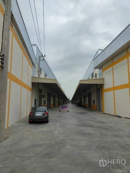 Warehouse for rent in Krathum Baen, Samut Sakhon - Central driveway through the warehouse estate with parking and loading zones.