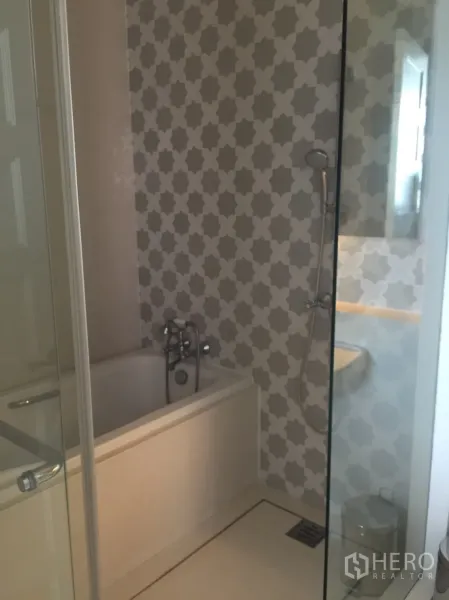 公寓 出租在Khlong Toei, Bangkok - 浴室带浴缸与手持花洒，几何纹墙面和玻璃隔断。