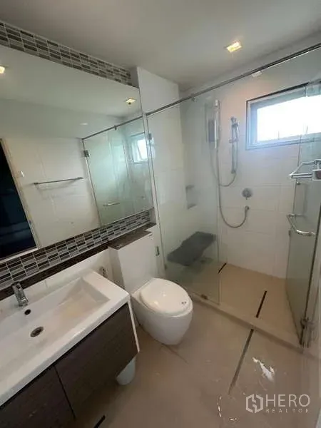 Detached House for rent or sale in Bang Kapi, Bangkok - Contemporary bathroom with glass-enclosed shower, vanity sink and wall mirror with natural light window.