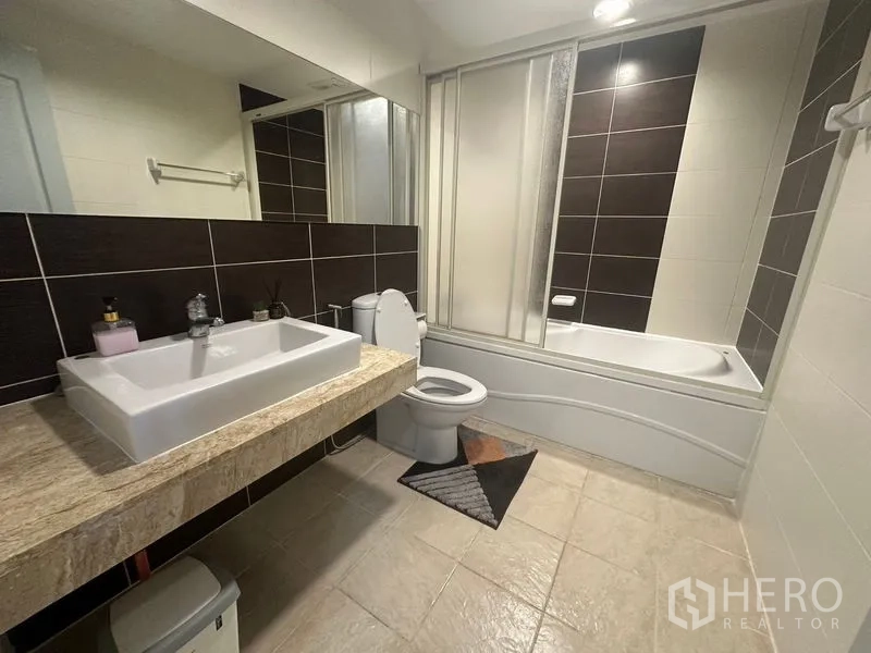 Condominium for rent in Watthana, Bangkok - Full bathroom with bathtub and glass screen, wide stone countertop and large mirror.