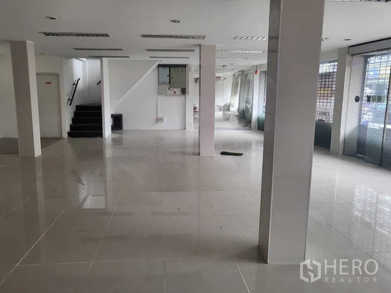 店屋 出租在Khlong Toei, Bangkok - 临街商铺一层开放式空间，亮面瓷砖地面、承重柱、楼梯与宽幅玻璃门面。
