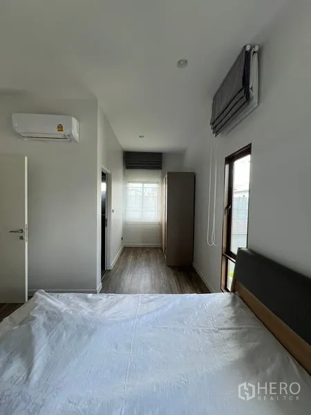 Detached House for rent in Bang Kapi, Bangkok - Bedroom view showing air conditioner, tall windows and wood floors.