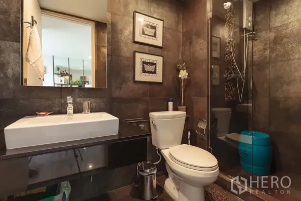 公寓 出租在Khlong Toei, Bangkok - 现代浴室，深色墙砖，玻璃淋浴间与悬浮洗手台。