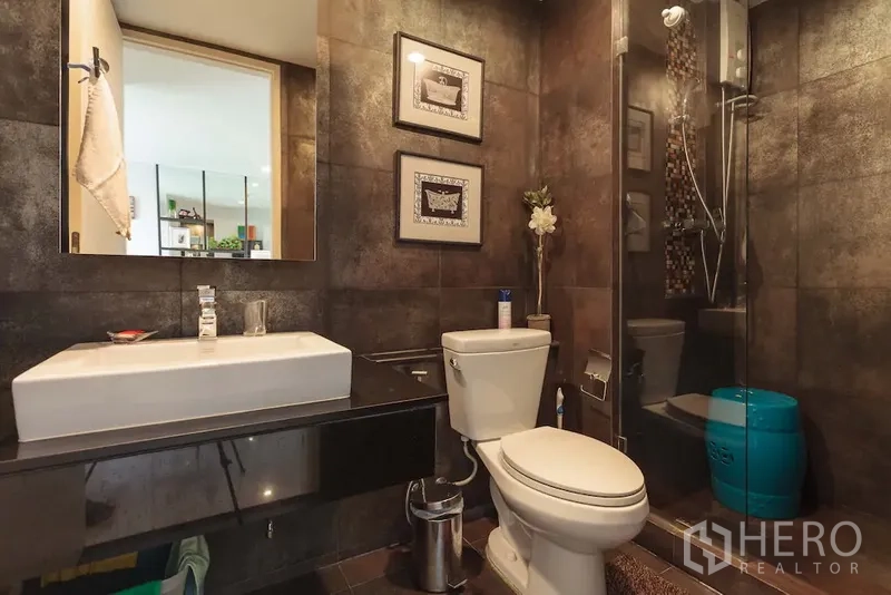 公寓 出租在Khlong Toei, Bangkok - 现代浴室，深色墙砖，玻璃淋浴间与悬浮洗手台。