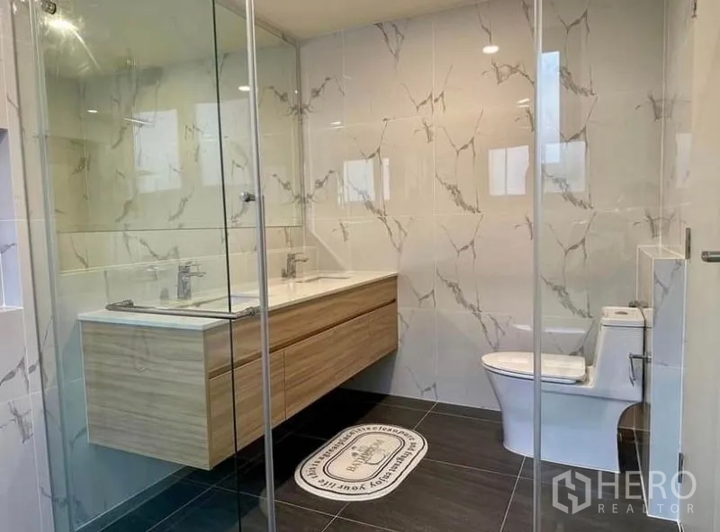 Detached House for rent in Bang Phli, Samut Prakan - Contemporary bathroom with double-sink vanity, glass shower and toilet on dark floor tiles.
