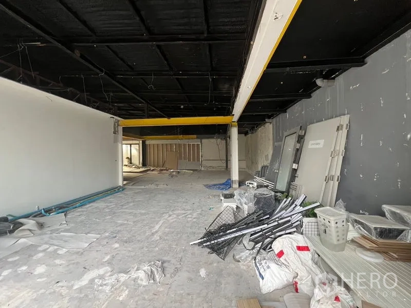 零售空间 出租在Watthana, Bangkok - 开放式室内施工中，黑色天花与黄色梁，水泥地面。