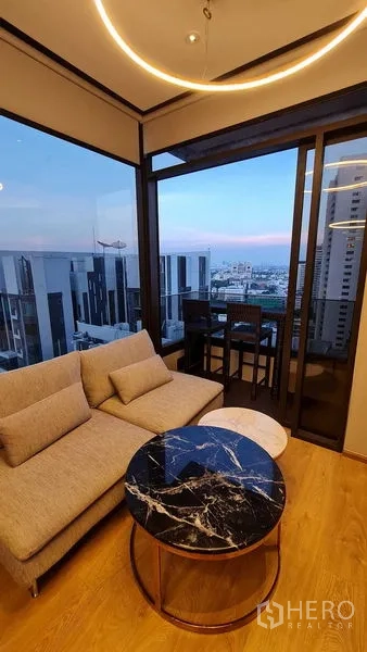 Condominium for rent in Watthana, Bangkok - Living room with sofa and round marble coffee table opening to a city-view balcony.