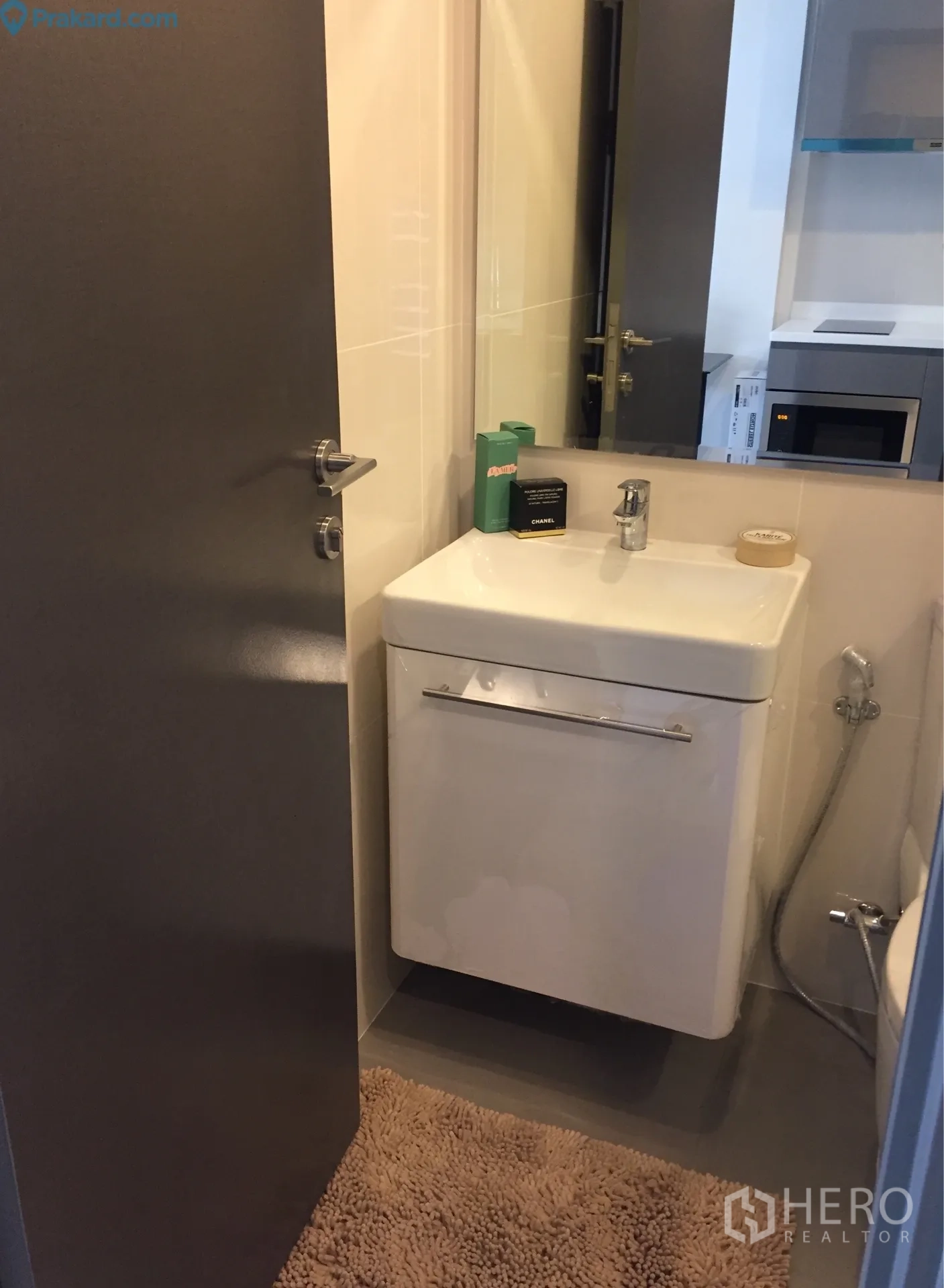 Condominium for rent in Ratchathewi, Bangkok - Modern bathroom vanity with mirror and door opening toward a kitchenette area.