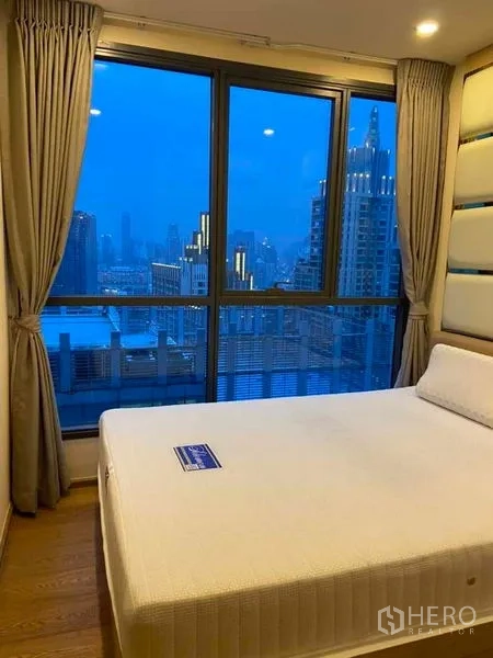 Condominium for rent or sale in Ratchathewi, Bangkok - Bedroom with large windows showcasing a night city view.