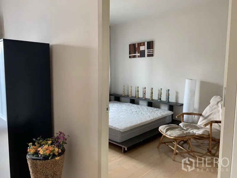 公寓 出租在Phaya Thai, Bangkok - 从走廊望向卧室，床垫、藤椅与装饰架，配色简约。