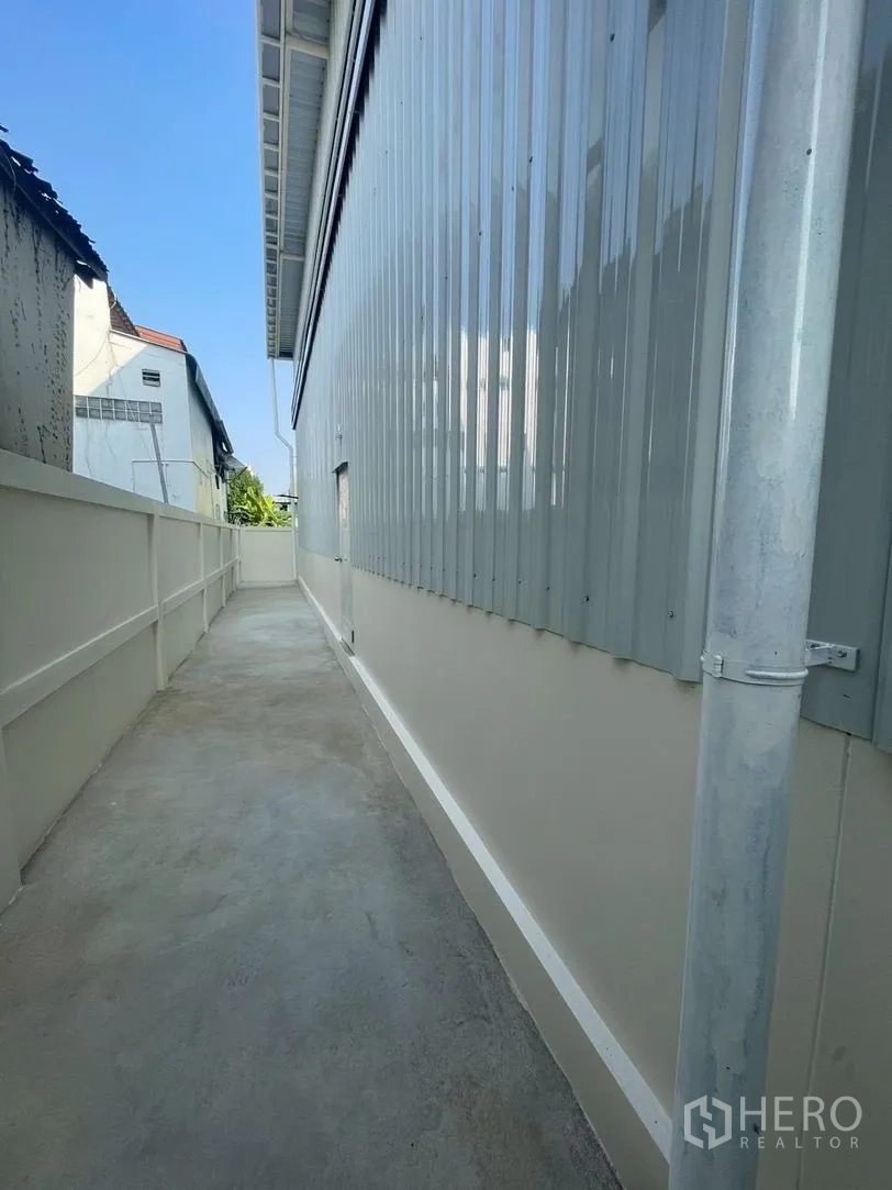 仓库 for rent in Prawet, Bangkok - 仓库金属墙旁的混凝土侧向通道。