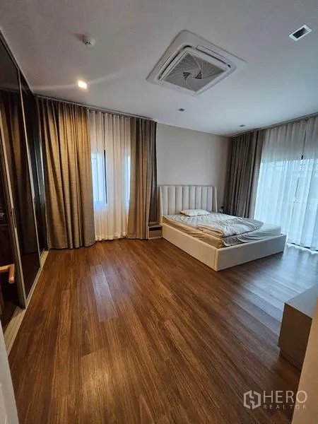 Detached House for sale in Mueang Pathum Thani, Pathum Thani - Primary bedroom with wood floors, large windows, sheer curtains and cassette air-con.