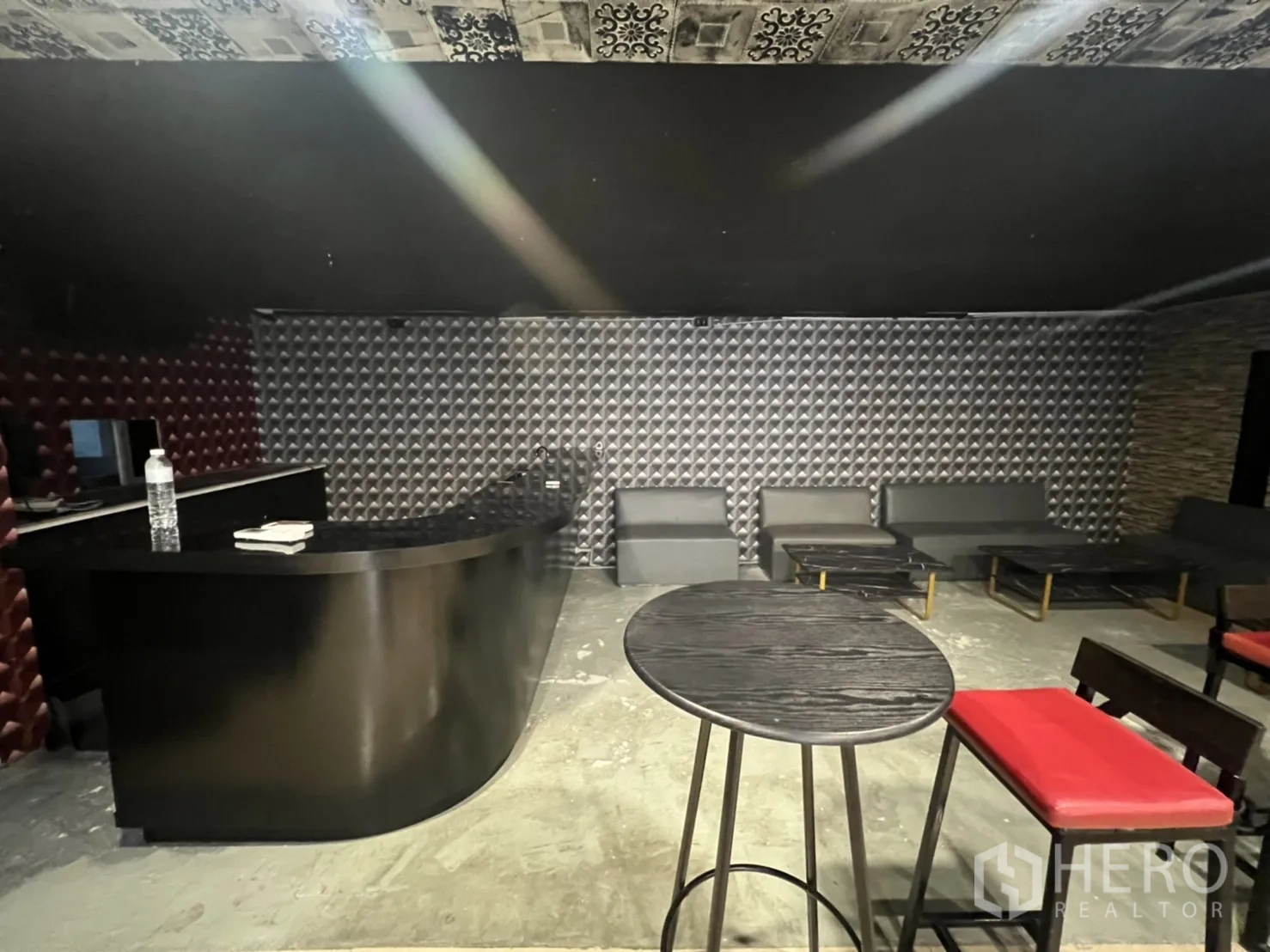 零售空间 出租在Watthana, Bangkok - 休息区，黑色弧形吧台、灰色沙发与纹理墙面。