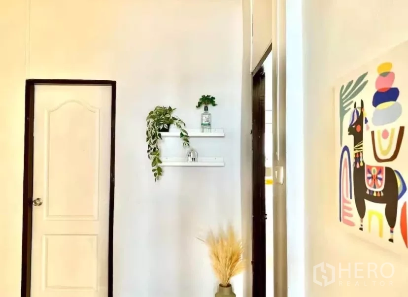 Townhouse for rent in Watthana, Bangkok - Hallway corner with floating shelves, greenery and colorful wall art.