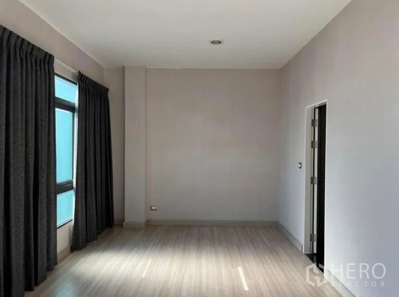 Townhouse for rent or sale in Bang Kho Laem, Bangkok - Sunlit room with corner windows, dark drapes and entry to a bathroom.