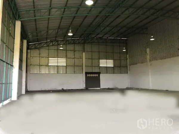 Factory for rent in Pathum Thani - Spacious warehouse interior featuring a high steel truss roof, hanging lights, concrete floor and ventilation windows.