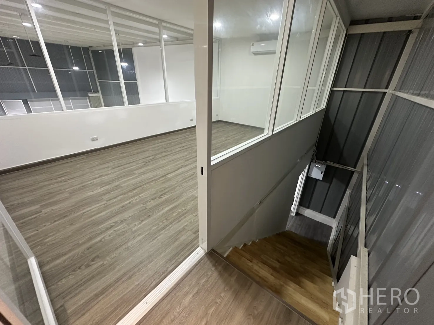 Warehouse for rent in Suan Luang, Bangkok - Staircase to mezzanine office with large interior windows, AC unit and wood‑tone steps and flooring.