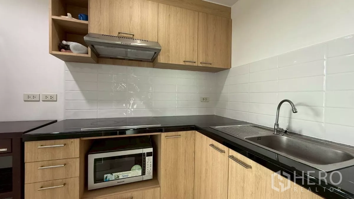 คอนโด ขายในYan Nawa, Bangkok - ครัวบิลท์อิน ตู้ไม้ เคาน์เตอร์สีดำ เตาไฟฟ้า และผนังกระเบื้องสีขาว