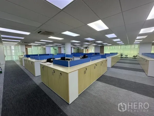 Office Space for rent - Open-plan office with blue-partition workstations, storage cabinets, carpet tiles, and LED ceiling lights.