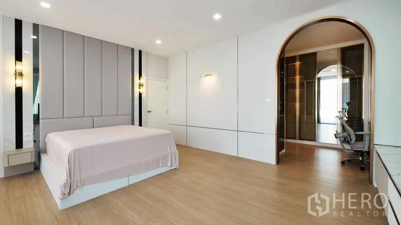 Detached House for rent or sale in Thanyaburi, Pathum Thani - Large master bedroom with wood flooring and arched entry to a walk-in closet area.