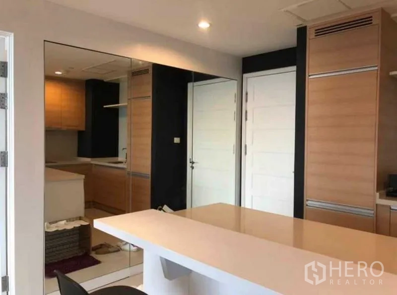 Condominium for sale in Khlong Toei, Bangkok - Kitchen area with mirrored wall, storage cabinets and white internal doors.