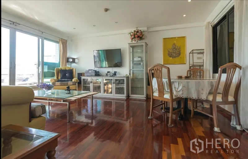 Condominium for rent in Pathum Wan, Bangkok - Open-plan living and dining area with TV console, large windows and polished hardwood flooring.