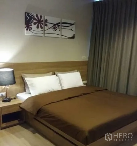 Condominium for rent in Sathon, Bangkok - Primary bedroom with wood headboard, brown bedding, bedside lamp and blackout curtains.