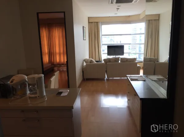 Condominium for rent in Khlong Toei, Bangkok - Bright living room with bay window, beige sofas and TV overlooking Bangkok skyline.