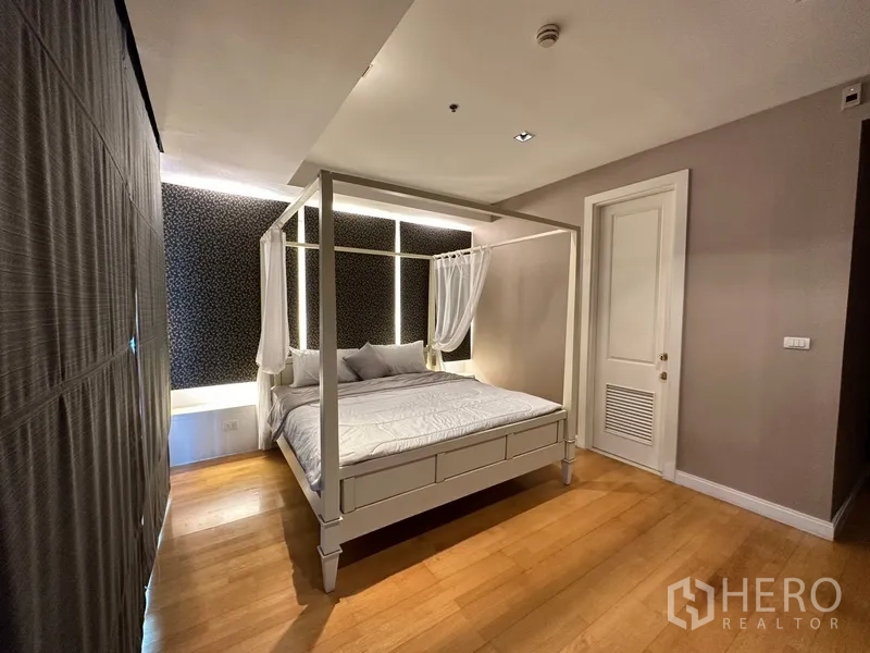 Condominium for rent in Pathum Wan, Bangkok - Spacious master bedroom with canopy bed, wood floors and accent wall.