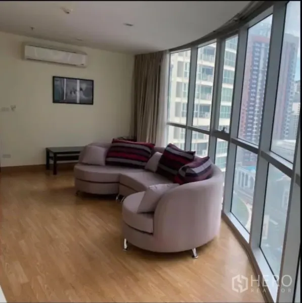 Condominium for rent in Watthana, Bangkok - Bright living room with curved sofa and floor-to-ceiling windows offering city views.