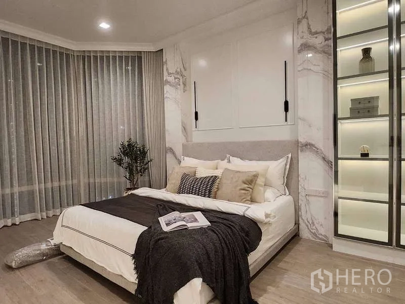 Condominium for sale in Watthana, Bangkok - Cozy bedroom corner with large windows, sheer curtains and a lighted wardrobe.