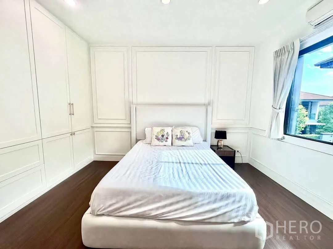 Detached House for rent in Bang Kapi, Bangkok - Bright bedroom with white paneled walls, built-in wardrobes and a bed.